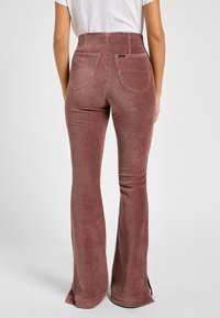 Pantalones acampanados de sarga en rosa empolvado con canalé vertical, talle alto, dos bolsillos traseros y aberturas en los laterales del dobladillo para un detalle adicional.