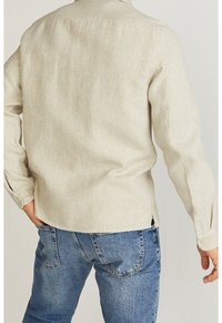 Lyse beige langærmet skjorte i tekstureret linned med sideskår og knapmanchetter, parret med blå denimjeans.