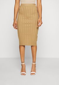 Pletená tužková sukně ve světle hnědé barvě s vertikálním žebrovaným vzorem; délka po střed lýtek, elastický pas; spárováno s bílými sandály na podpatku.