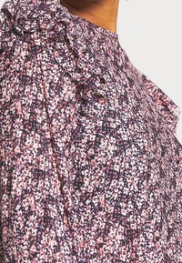 Bluse mit floralem Druck und Rüschendetails an den Schultern. Aus leichter Stoffqualität in einer Mischung aus Rosa, Weiß und Marineblau. Runder Ausschnitt.