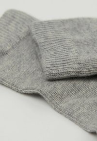 Graue Stricksocken mit geripptem Abschluss, weicher Textur und subtilen Mustern, die im gesamten Stoff sichtbar sind. Eine Nahaufnahme hebt die Details hervor.