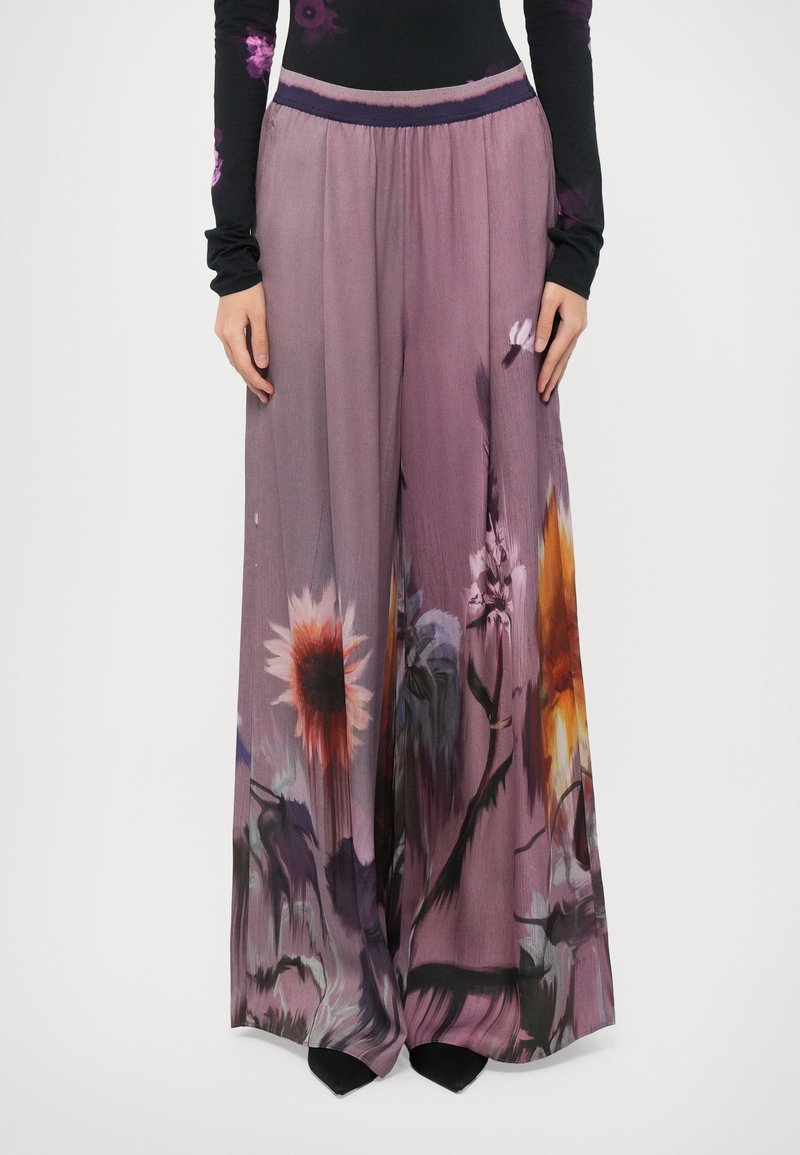 Pantaloni a gamba larga in tessuto fluido, caratterizzati da un gradiente di colore viola e una stampa floreale in tonalità di arancione, giallo e blu. Vita elasticizzata.