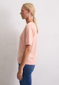 Pull court rose à manches courtes avec une coupe décontractée, col et ourlet côtelés, texture lisse et fentes sur les côtés, associé à un jean bleu foncé.