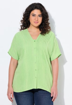 Camicia verde chiaro a maniche corte con scollatura a V, caratterizzata da una texture a righe verticali e cinque bottoni lungo la parte anteriore. L'orlo è arrotondato.