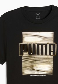 Černé bavlněné tričko s pozlaceným grafickým designem obsahujícím text "PUMA" a vodorovné čáry, s frází "PERFORMANCE SINCE 1948" pod tím.