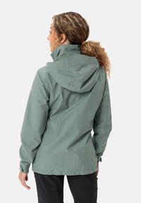 Giacca outdoor verde, con texture e cappuccio, presenta una chiusura con zip, polsini regolabili e una vestibilità rilassata, adatta a diverse condizioni atmosferiche.