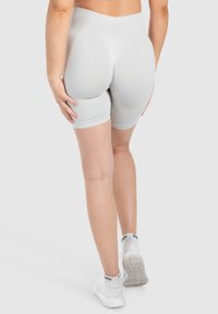 Pantaloni corti grigi chiari con un alto punto vita e un design aderente, caratterizzati da elementi curvi sul retro, realizzati in materiale elasticizzato.