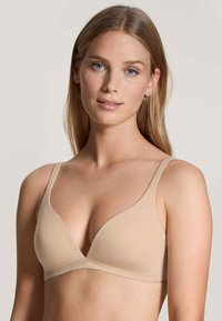 Beige, seamless, soft fabric bra with a triangular cup design and adjustable straps. Minimalistic style, smooth texture, no visible hardware.