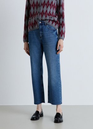 Persona che indossa jeans blu corti, mocassini neri e un maglione argyle rosso e grigio con bottoni.