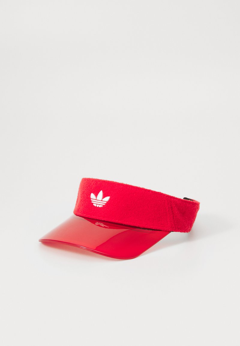 Sarkans vizieris ar mīkstu, teksturētu joslu un spīdīgu vizieri. Priekšpusē atrodas balts Adidas logo. Aizmugurē ir regulējams siksniņa.