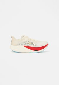 Ανοιχτό μπεζ παπούτσι για τρέξιμο με πλεκτό επάνω μέρος, κόκκινες και μπλε λεπτομέρειες, παχιά λευκή μεσαία σόλα και εμφανές λογότυπο στο πλάι.