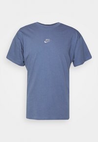 Camiseta de manga corta azul hecha de algodón, con cuello redondo y un pequeño logo blanco de Nike en el pecho. Diseño simple y de color sólido.
