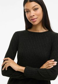 Robe noire en tricot côtelé avec un col ras du cou et des manches longues, présentant une surface texturée et une silhouette ajustée.