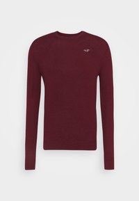 Burgundy stickad tröja med långa ärmar, ribbade ärmslut och nederkant, har en liten logotyp på vänster bröst, tillverkad av mjukt material.