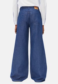 Weit geschnittene Jeans in Dunkelblau mit strukturierter Oberfläche. Verfügt über zwei Gesäßtaschen und ein hellbraunes Leder-Branding-Patch am Bund.