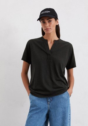 Donkergroene T-shirt met korte mouwen en een kraagloze halslijn, subtiele naden, gecombineerd met lichtblauwe spijkerbroek en een zwarte pet.