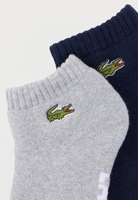 Δύο ζευγάρια κάλτσες μέχρι τον αστράγαλο: ένα γκρι και ένα ναυτικό μπλε, καθένα με ένα πράσινο λογότυπο κροκοδείλου κεντημένο κοντά στο μανσέτα. Απαλή, ριμπ υφή.