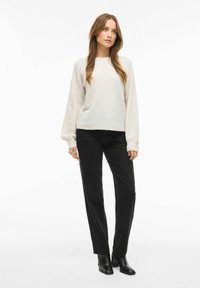 Gaiši dzijas džemperis off-white krāsā ar smalku rakstu, apvienots ar melnām taisnām biksēm un melnām potīšu zābakiem.