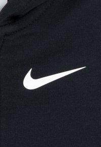 Svart stoff med en glatt tekstur har en fremtredende hvit Nike-swoosh logo i midten, som representerer merkeidentitet og designelementer.