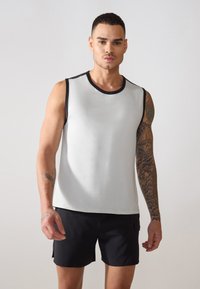 Ärmelloses graues Sporttanktop mit einem schwarzen Rundhalsauschnitt, das eine glatte Textur und flache Nähte aufweist. Getragen mit schwarzen Shorts.