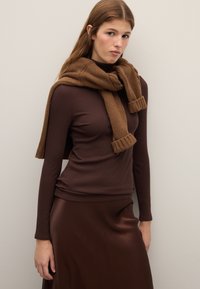 Brown knit scarf draped over a ribbed brown long-sleeve top, paired with a smooth, dark brown satin skirt. Neutral background.