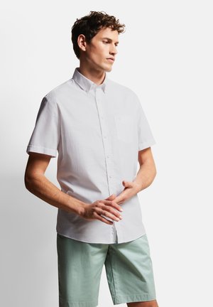 Weißes Kurzarm-Hemd mit Knöpfen und kleiner Tasche, kombiniert mit mintgrünen Shorts. Baumwollmaterial, glatte Textur, lässiges Design.