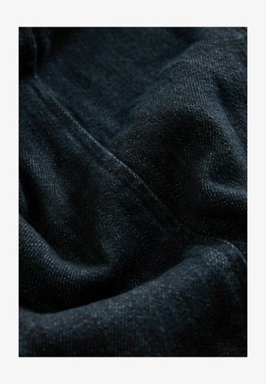 Tessuto denim blu scuro, caratterizzato da una consistenza liscia con una leggera lucentezza, piegato per mostrare un sottile motivo di tessitura diagonale e dettagli di cucitura.