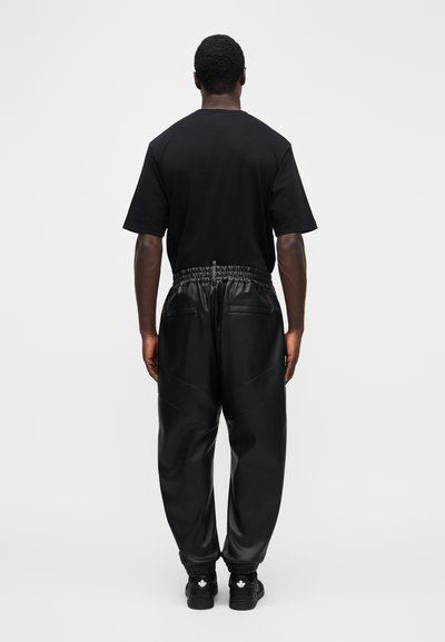 Černé bavlněné tričko s krátkými rukávy a volnějším střihem, doplněné černými koženými tepláky s elastickým pasem a dvěma zadními kapsami.