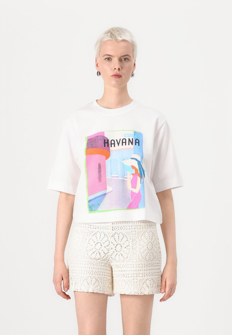 Tricou alb scurt cu un grafic colorat al unei femei în Havana, cu textul "CUBA" și "HAVANA". Asociat cu un șort alb cu o pată complexă.