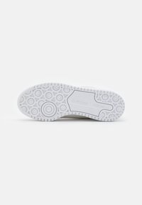 White sneaker sole with textured rubber, featuring circular patterns and a smooth central area. Branding visible on the side.