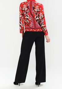 Long-sleeve red blouse featuring floral embroidery in pink, white, and blue, paired with black wide-leg trousers. High-heeled black shoes visible.