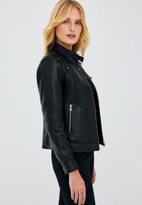 Zwarte leren motorjack met een hoge kraag, ritssluiting aan de voorkant en zijzakken. Heeft een gladde textuur en een op maat gemaakte pasvorm.