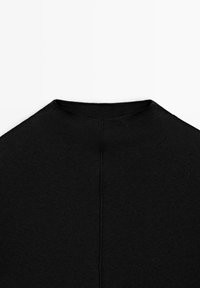 Black knitted top featuring a high neckline, smooth texture, and a central seam down the back. Simple, fitted design.