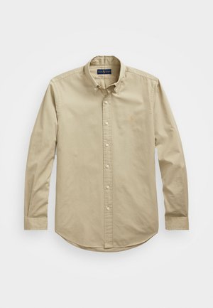 Chemise beige à manches longues avec boutons, col boutonné et un petit logo brodé sur le côté gauche de la poitrine.