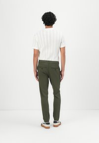Polo de punto blanco de manga corta con un patrón texturizado, combinado con pantalones ajustados en verde oliva y zapatillas blancas con detalles en negro.