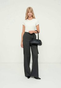 Μαύρη τσάντα χειρός με στρογγυλό σχήμα και κοντά χερούλια, συνδυασμένη με ένα εφαρμοστό λευκό τοπ και γκρι παντελόνι με ψηλή μέση και φαρδιά γραμμή.