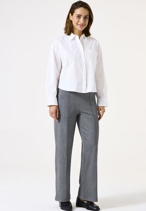 Chemise blanche à col classique associée à un pantalon gris à rayures verticales, avec une coupe droite et une texture subtile. Des chaussures noires complètent la tenue.