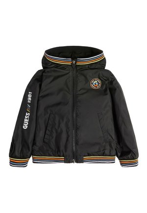 Veste noire à capuche avec fermeture éclair, poignets et col rayés, texte "GUESS 1981" sur la manche, et logo rond sur la poitrine.
