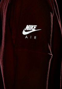 Sudadera Nike Air en burdeos oscuro, con una textura perforada y un logo Nike blanco en la manga de manera prominente.
