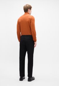 Oranžový rolák z mäkkého materiálu, spárovaný s čiernymi nohavicami s elastickým pásom. Jednoduchý, minimalistický dizajn bez viditeľných vzorov.