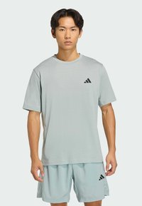 Svetlomodré atletické tričko s krátkymi rukávmi a okrúhlym výstrihom. Na ľavej strane na hrudi je čierne logo Adidas. Jemná textúra tkaniny.