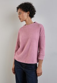 Helles rosa, flauschiges Sweatshirt mit weitem Ausschnitt und Dreiviertelärmeln, kombiniert mit dunklen Jeans. Weiche Textur, lockere Passform.