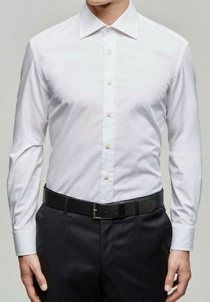 Chemise blanche à manches longues avec un col ouvert, associée à un pantalon sombre et une ceinture noire avec une boucle en argent.