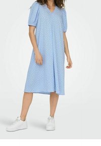  Vaaleansininen mekko, jossa on lyhyet puffihihat, V-pääntie ja rento leikkaus. Mekossa on hillitty kuvio ja se ulottuu puoleenväliin sääriä. Yhdistettynä valkoisiin tennareihin.