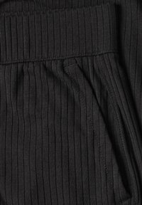 Gros plan d'un tissu côtelé noir avec un détail de couture pliée et une ouverture de poche visible sur le côté droit.