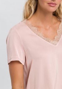 Blouse rose clair à manches courtes, dotée d'un décolleté en V orné d'une délicate bordure en dentelle. Tissu lisse avec un léger éclat.
