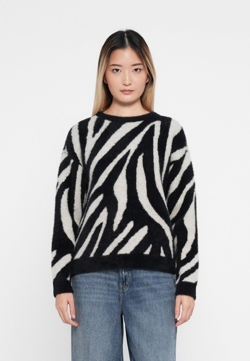 Sort og creme-stribet zebra-sweater, lavet af blødt, fuzzy materiale. Har rund hals og lange ærmer, parret med lyseblå denimjeans.