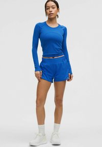 Sinine pikkade varrukate sporditopp ja sellele sobivad lühikesed püksid kergetest materjalidest. Pükstel on elastne talje. Kujunduse lõpetavad valged tossud.