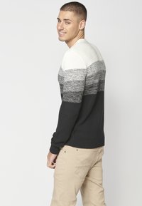 Pulover tricotat cu un model gradient în alb, gri și negru. Design structurat cu tiv și manșete cu cordon, purtat cu pantaloni bej.