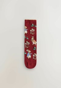 Red socks featuring a whimsical illustration of rabbits and greenery, with detailed patterns including candles and leaves. Cotton blend material.